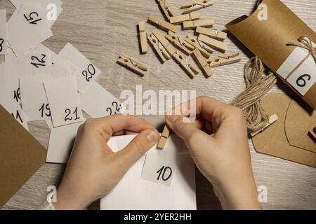 Méconnaissable jeune femme bâtons le numéro sur le sac d'artisanat, se fixe avec la pince à linge. Femme faisant du papier kraft pour le calendrier de l'AVENT fait maison avec votre Banque D'Images