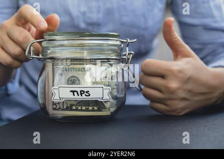 Femme méconnaissable tenant pot en verre plein de billets de banque en dollars américains avec DES CONSEILS DE texte. Préparation du pouce vers le haut pour économiser de l'argent. Modéré Banque D'Images