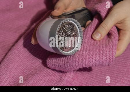 Femme utilisant le rasoir anti-boulochage à la maison. Dispositif pour raser des vêtements. Rasoir à tissu anti-peluche. Détartrant de peluches pour chandail portable électrique Banque D'Images