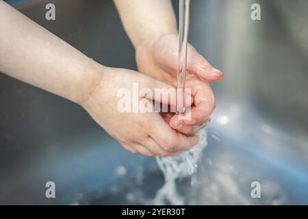 Gros plan de deux mains d'enfants gonflées pendant le moment de lavage des mains avant le déjeuner, faisant de la mousse avec du savon sous un jet d'eau dans l'évier Banque D'Images
