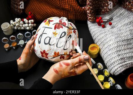 BRICOLAGE. Faites-le vous-même. Une femme peint des décorations d'action de grâce sur la citrouille d'orange pour Halloween. Récolte d'automne. Chandail maison confortable. Pinceau Banque D'Images