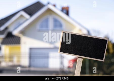 Panneau noir vierge contre le nouveau bâtiment de maison modèle de maquette vide étiquette de panneau noir Maison à louer. Maison à vendre. Inscrivez-vous devant la nouvelle maison. Copier Banque D'Images