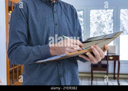 Inspecteur tenant un cahier à la main. Gros plan des mains de l'homme prenant des notes tout en se tenant à l'intérieur pendant l'inspection de la maison, fond intérieur de la maison Banque D'Images