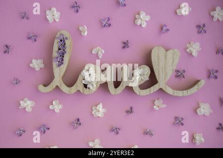 Mot en bois AMOUR et fleurs lilas sur fond violet rose. St. Concept de Saint-Valentin, d'amour ou de mariage. Composition de fond romantique. Pastel Banque D'Images