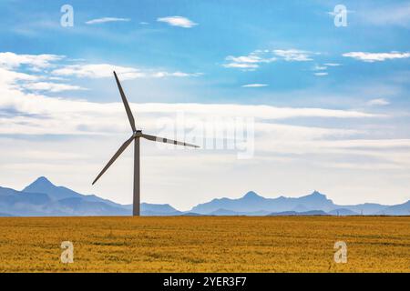 Une éolienne, avec une nacelle et trois pales au sommet d'une monopole, est vue sur des terres agricoles rurales en Saskatchewan, au Canada. Avec des montagnes à l'horizon Banque D'Images