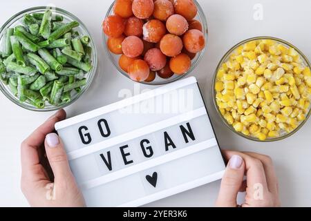 Visionneuse avec texte GO VEGAN trois bols de légumes surgelés nourriture de maïs jaune, haricots verts, tomates rouges. Couleurs des feux de circulation. Pré-récolte des aliments Banque D'Images