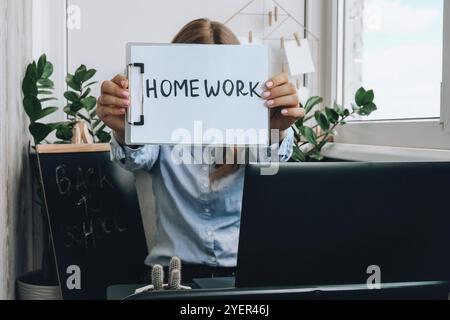 Jeune femme enseignante assise au bureau et utilisant un ordinateur portable montrant LE TEXTE DU DEVOIR à la maison. e éducation Retour à l'école. Cours en ligne sur l'apprentissage des élèves. Distan Banque D'Images