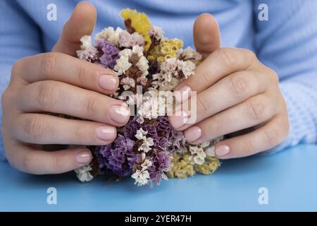 Femme mains manucurées, ongles beiges élégants. Gros plan des ongles manucurés de la main féminine en pull bleu sur fond bleu. Style hiver ou automne de na Banque D'Images