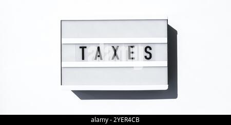 Tableau lumineux sur fond blanc avec les mots TAXS en lettres noires. Devise, espèces Banque D'Images