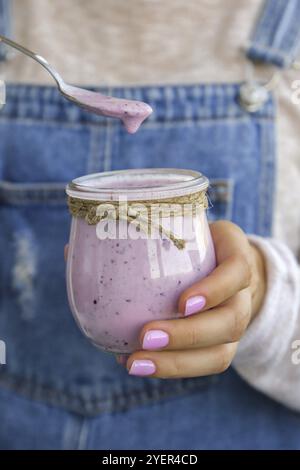 Mains de femmes portant du smoothie aux myrtilles nappées de bleuets. Femme mangeant un verre de boisson de smoothie aux protéines de petit déjeuner à base de blueberri brut de puroseau Banque D'Images