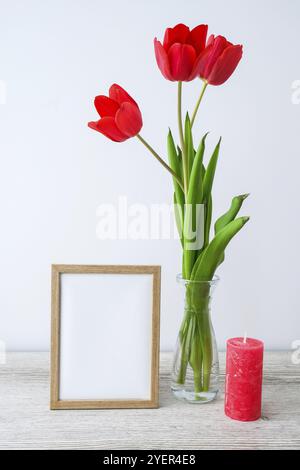 Maquette des fêtes. Fleurs tulipes dans vase en verre avec cadre photo décor sur table en bois arrière-plan mur à la maison, gros plan, Fête des mères Womans Valentines Banque D'Images