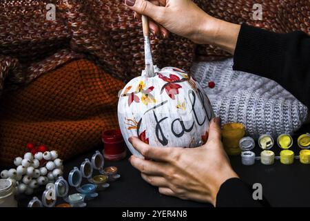 BRICOLAGE. Faites-le vous-même. Une femme peint des décorations d'action de grâce sur la citrouille d'orange pour Halloween. Récolte d'automne. Chandail maison confortable. Pinceau Banque D'Images