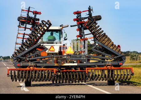 Un agriculteur a vu la conduite d'un grand tracteur industriel de derrière, avec l'extension du travail du sol charrue rotative et pièce jointe pour la gestion des terres agricoles Banque D'Images