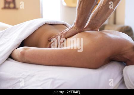 Une jeune femme recevant un massage Santosh dans un environnement confortable à la maison. Massage corporel spa. Mains fortes du masseur masculin professionnel faisant le massa dos doux Banque D'Images