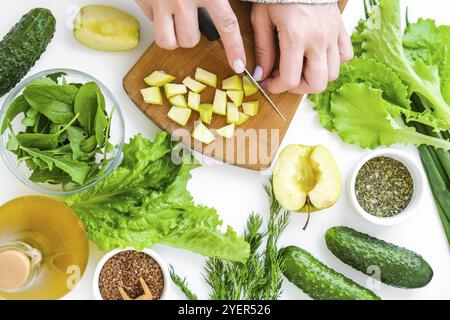 Femme cuisant de la salade de légumes verts frais et des herbes. Cuisiner un régime alimentaire sain ou des aliments végétariens. Les mains des femmes coupent la pomme sur la planche à découper entourée b Banque D'Images