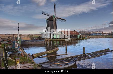 Oilmill de Zoeker sur le Zaanse Schans un jour d'hiver calme sous un ciel bleu avec des nuages dispersés avec des troncs d'arbres et des bateaux au premier plan. Banque D'Images