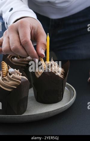 Les mains des femmes font de délicieux petits gâteaux au chocolat avec de la crème sur fond sombre. Trois muffins au chocolat. Gâteau d'anniversaire préparation de fête. Choco. Maison Banque D'Images