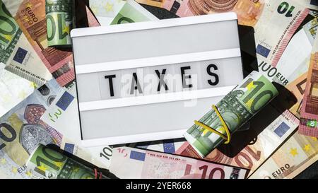 Tableau lumineux avec mot TAXS en lettres noires autour des billets en euros. Paiement d'impôt et présentation de déclarations. Argent, affaires, finances, investissement, économie Banque D'Images