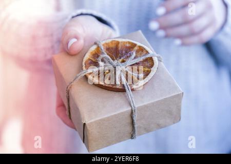 Femme donnant boîte avec des cadeaux du nouvel an, enveloppé dans du papier artisanal et décoré avec des tranches d'orange sèches. Concept de vacances et de cadeaux. Fait à la main écologique Banque D'Images