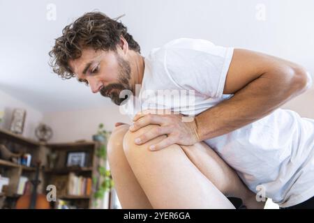Masseuse professionnelle de mi-âge offrant un massage des jambes à un homme fort. Sportif recevant un massage relaxant dans l'environnement confortable de la maison Banque D'Images