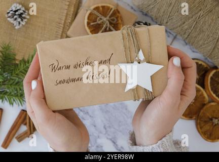 Voeux chaleureux et bonhomme de neige inspiration blague citation phrase femme faisant boîte avec les cadeaux du nouvel an, enveloppé dans du papier artisanal et décoré de soutien-gorge de sapin Banque D'Images