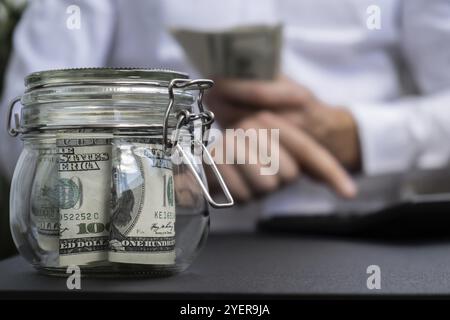 Billet de banque dollar économisant de l'argent dans le pot en verre. Homme méconnaissable calculer l'argent sur la calculatrice consommation modérée et économie collecte d'argent conseils bus Banque D'Images