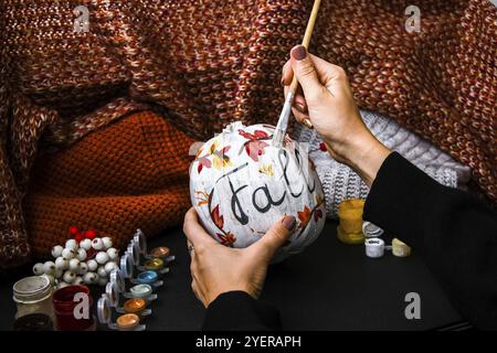 BRICOLAGE. Faites-le vous-même. Une femme peint des décorations d'action de grâce sur la citrouille d'orange pour Halloween. Récolte d'automne. Chandail maison confortable. Pinceau Banque D'Images