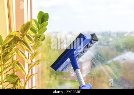 La main de l'employé dans un gant de protection en caoutchouc nettoie la fenêtre avec de la mousse et un extracteur.Nettoyage général du ressort.Concept de ménage et de ménage Wiper avec un Banque D'Images