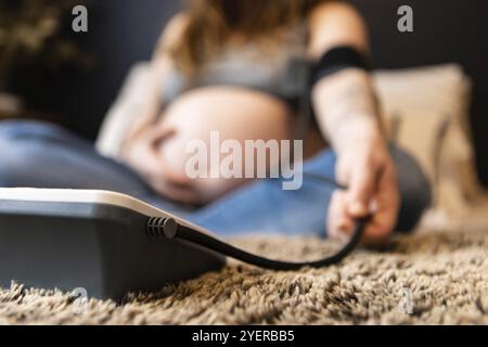 Gros plan et plan de mise au point sélective abstrait d'une femme enceinte floue proche de l'accouchement mesurant la pression artérielle sur un sphygmomanomètre à la maison Banque D'Images