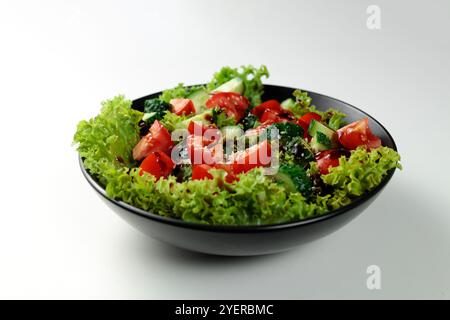 Salade de légumes de tomates, concombres, oignons, laitue habillée d'une vinaigrette aromatique dans une plaque noire sur fond blanc Banque D'Images