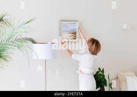 Femme accrochant une photo au mur dans la chambre. Design intérieur Banque D'Images