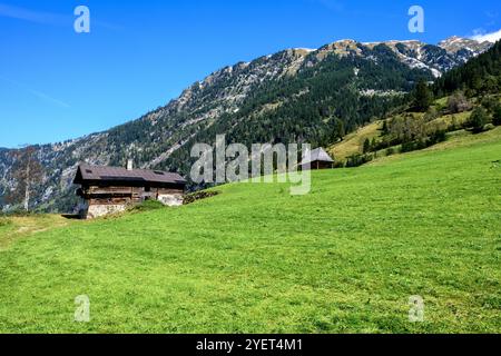 Sur une prairie alpine escarpée se dresse une très vieille ferme abandonnée avec une petite église en arrière-plan. Banque D'Images