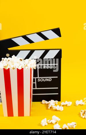 Image verticale de pop-corn avec clapet de film en bois sur un fond jaune avec pop-corn dispersé autour, cinéma et concept de divertissement Banque D'Images