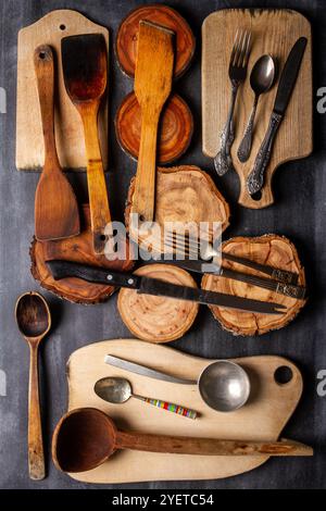 Vieilles planches à découper en bois, tranches de tronc d'arbre et ustensiles de cuisine sur fond noir de tableau noir. Pose à plat. Vue de dessus. Concept alimentaire. Banque D'Images