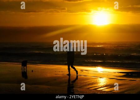 Île de Palms, États-Unis. 30 octobre 2024. Un homme et son chien silhouettés par une spectaculaire promenade au lever du soleil le long de Front Beach, le 30 octobre 2024 à Isle of Palms, Caroline du Sud. Un temps ensoleillé et chaud est prévu pour le pays bas pour les prochaines semaines. Crédit : Richard Ellis/Richard Ellis/Alamy Live News Banque D'Images