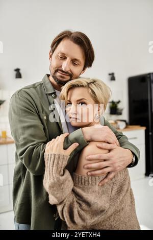 Un couple s'embrasse tendrement dans leur cuisine, profitant d'un moment calme et intime ensemble. Banque D'Images