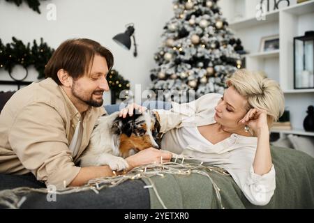 Un couple profite d'un moment chaleureux sur le canapé avec leur chien, décoré pour les vacances. Banque D'Images