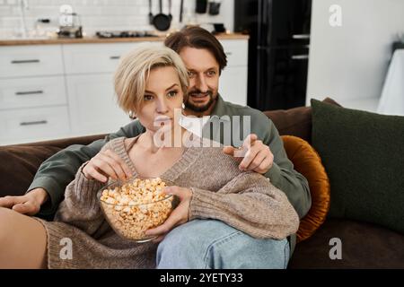 Un couple partage un moment tendre sur le canapé, profitant du pop-corn et d'une soirée cinéma à la maison. Banque D'Images