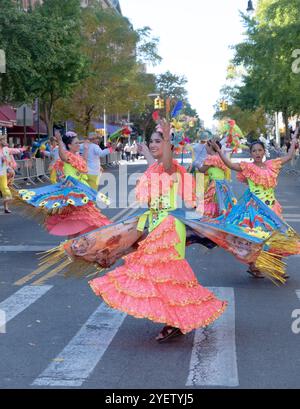 Les danseurs en robes orange colorées effectuent un parcours complexe tout en marchant dans la Parade bolivienne Day à Jackson Heights, Queens, New York. Banque D'Images