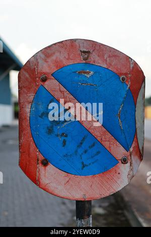 Gros plan d'un panneau No parking délavé et rouillé, mettant en valeur les textures et la décomposition urbaine. Banque D'Images
