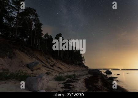 Scène nocturne en été, vue depuis la rive sablonneuse de l'île de Pedassaar jusqu'au continent estonien, ciel étoilé, voie lactée et pollution lumineuse. Banque D'Images