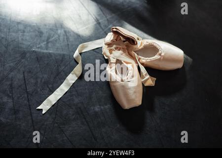 Plan d'arrière-plan de chaussures de pointe beige satiné décoré avec des rubans élégants couchés au soleil sur le sol sombre dans le studio de danse, espace copie Banque D'Images