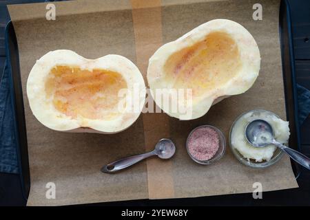 Citrouille blanche ensemencée et coupée en deux sur une poêle en feuille : moitiés d'une citrouille boule de neige frottées avec de l'huile de noix de coco et saupoudrées de sel rose sur du papier parchemin Banque D'Images