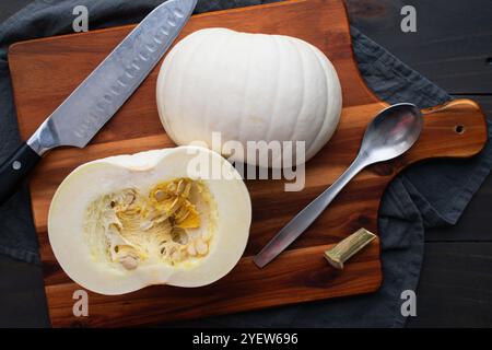 Citrouille à tarte blanche coupée en deux sur une planche à découper : préparation pour retirer les graines et la pulpe d'une citrouille boule de neige avec un couteau de chef et une cuillère Banque D'Images