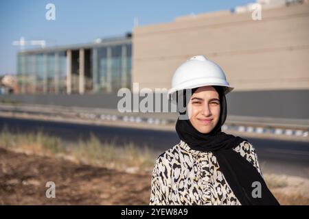 Une ingénieure confiante portant un casque de sécurité se tient sur place, supervisant les travaux de construction. Journée lumineuse et ensoleillée mettant en valeur le leadership et la profession Banque D'Images