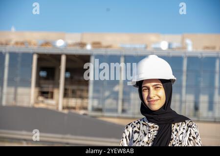 Une ingénieure confiante portant un casque de sécurité se tient sur place, supervisant les travaux de construction. Journée lumineuse et ensoleillée mettant en valeur le leadership et la profession Banque D'Images