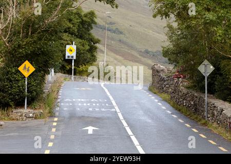 petite route rurale étroite jusqu'à une colline et autour d'un virage approchant l'école avec l'avance lente peinte sur la route avec des panneaux d'avertissement, comté de galway, république Banque D'Images