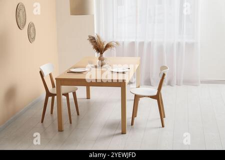 Vase d'herbe de pampa sur la table à manger et les chaises servies dans la pièce lumineuse Banque D'Images