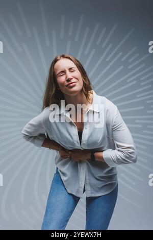 Jeune femme souriante dans une chemise blanche, t-shirt noir et jeans sur un fond gris. Portrait d'une femme brune elle a une douleur dans le foie, l'émotion Banque D'Images