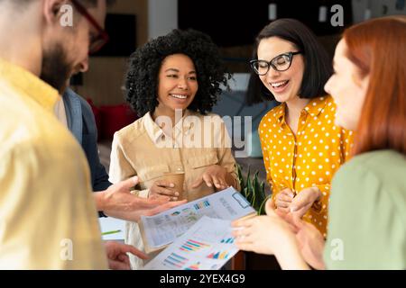 Une équipe diversifiée de professionnels des affaires sourit et rit tout en examinant des données financières positives dans un bureau bien éclairé Banque D'Images